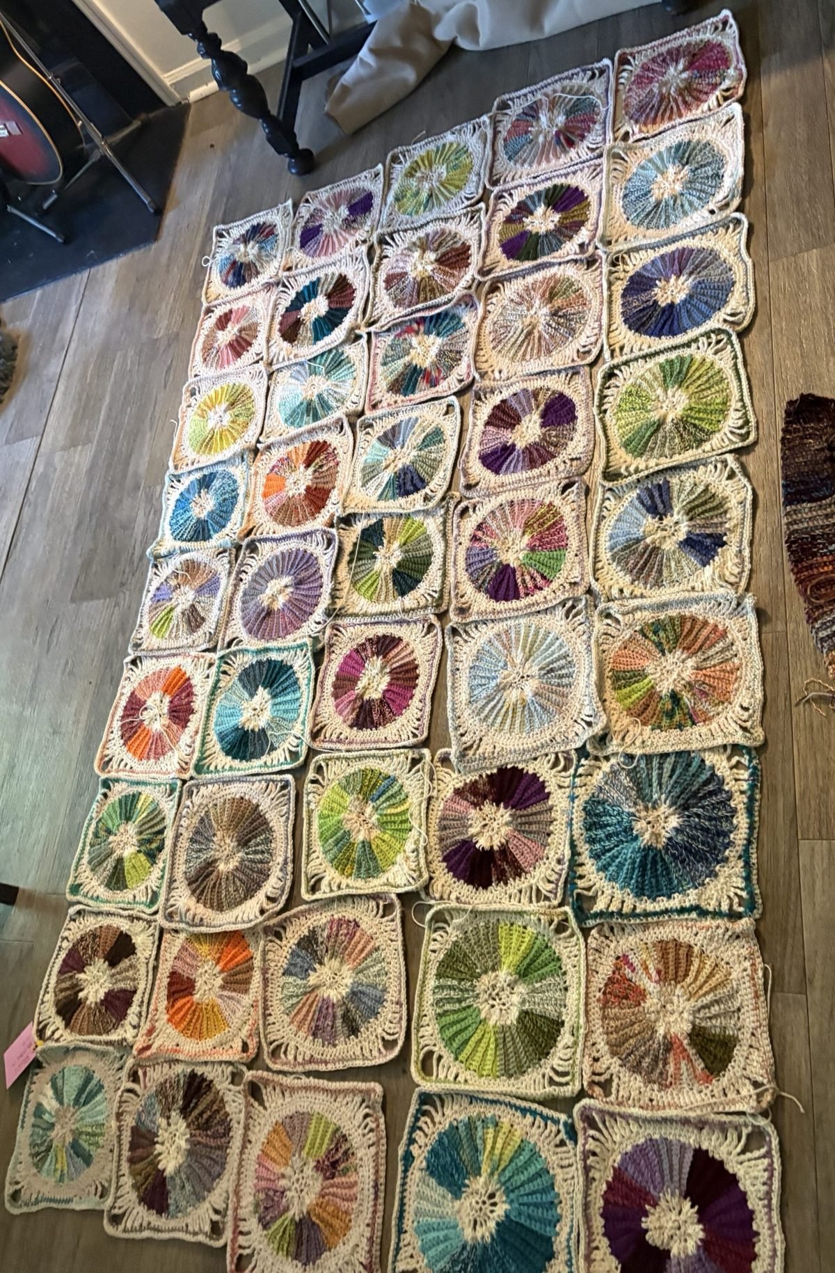 Forty-five Color Wheels squares laid out on a wood floor, each a burst of color inside a cream lace frame