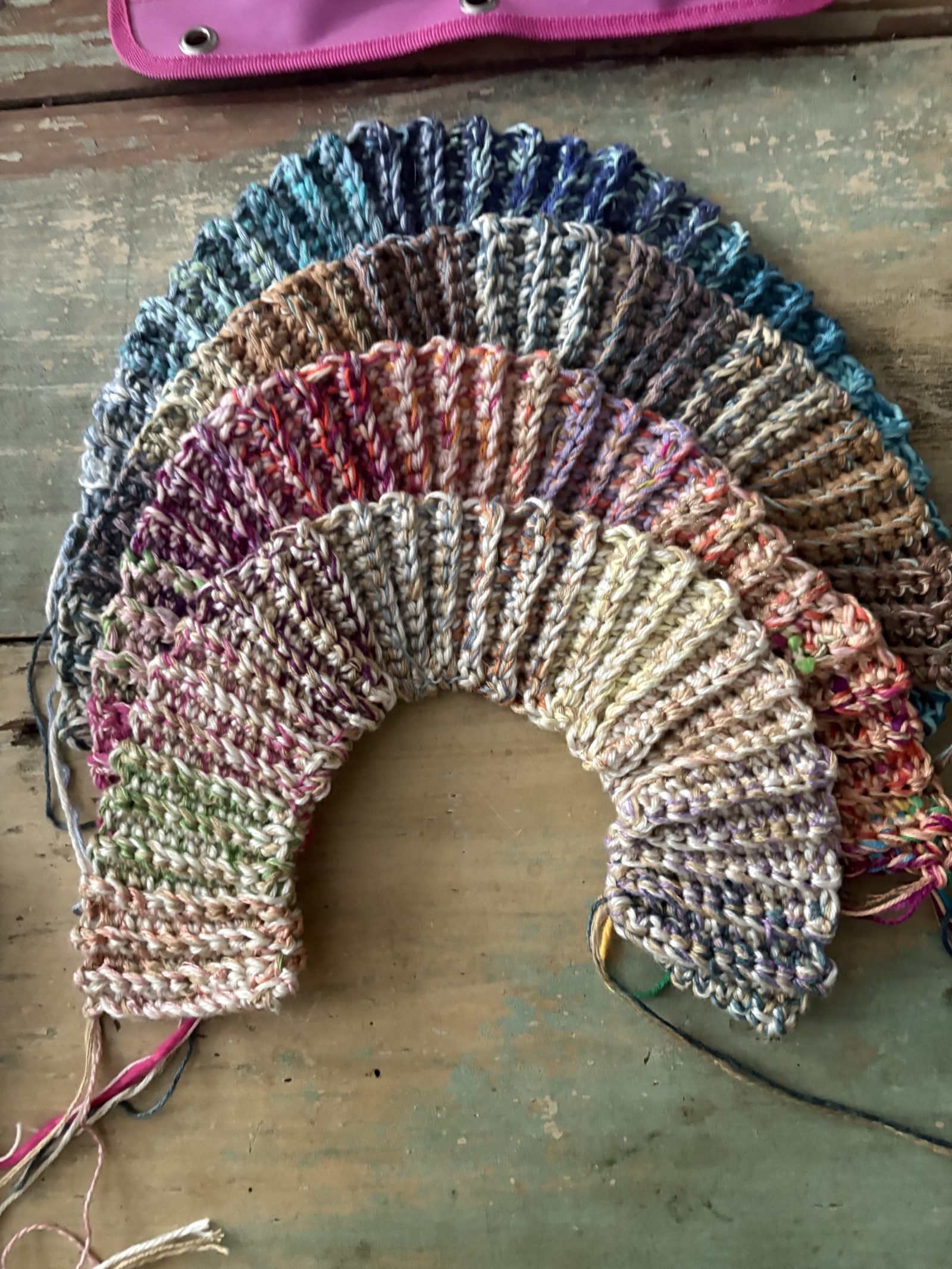 Four crocheted wheel strips stacked in a rainbow arc on a painted wood floor